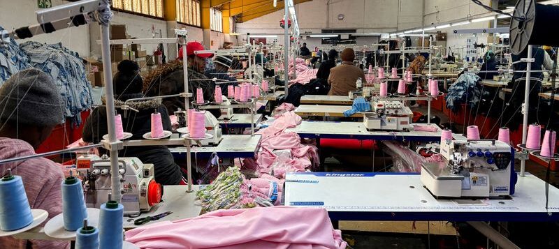 Workers operate sewing machines while others sit idle in a South African clothing factory.